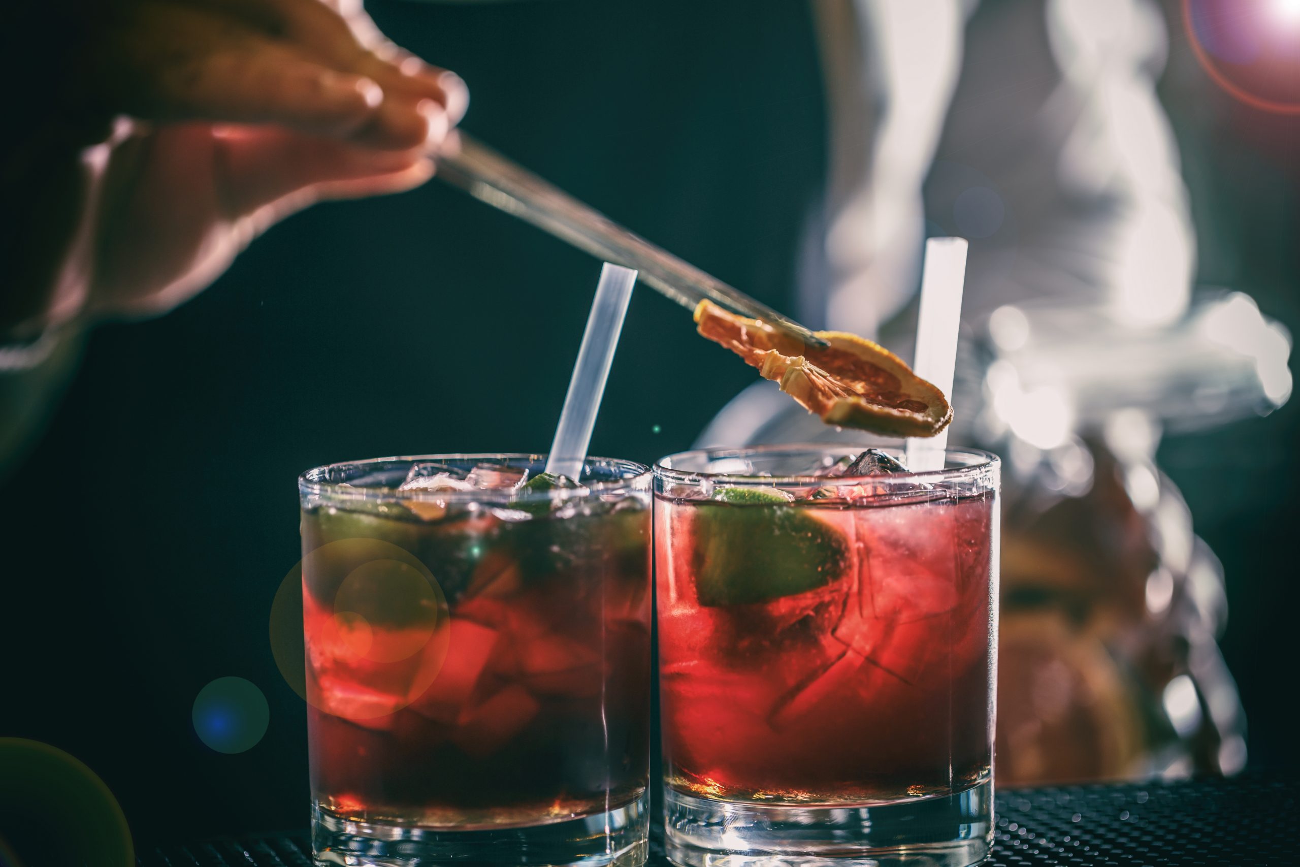 Bartender is adding lemon to the red cocktail at bar counter